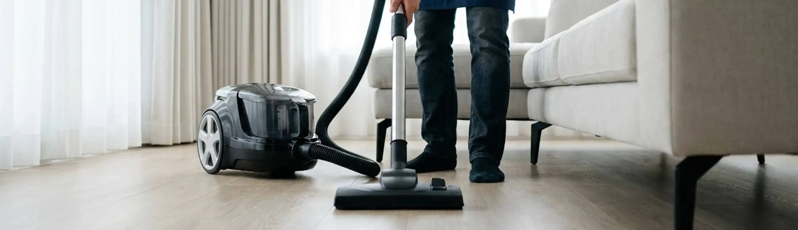 Professional house cleaner vacuuming a living room floor with a canister vacuum cleaner, Austin, TX.