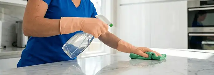 Maid service worker spraying and wiping a kitchen countertop with a microfiber cloth for sanitizing, Austin, TX.
