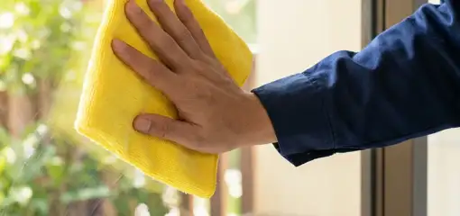 House cleaner wiping a glass window with a yellow microfiber cloth for streak-free cleaning, Austin, TX.